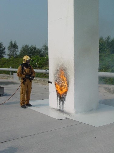 Een brandweercommandant houdt een gasbrander tegen een blok witte EPS voor een brandproef