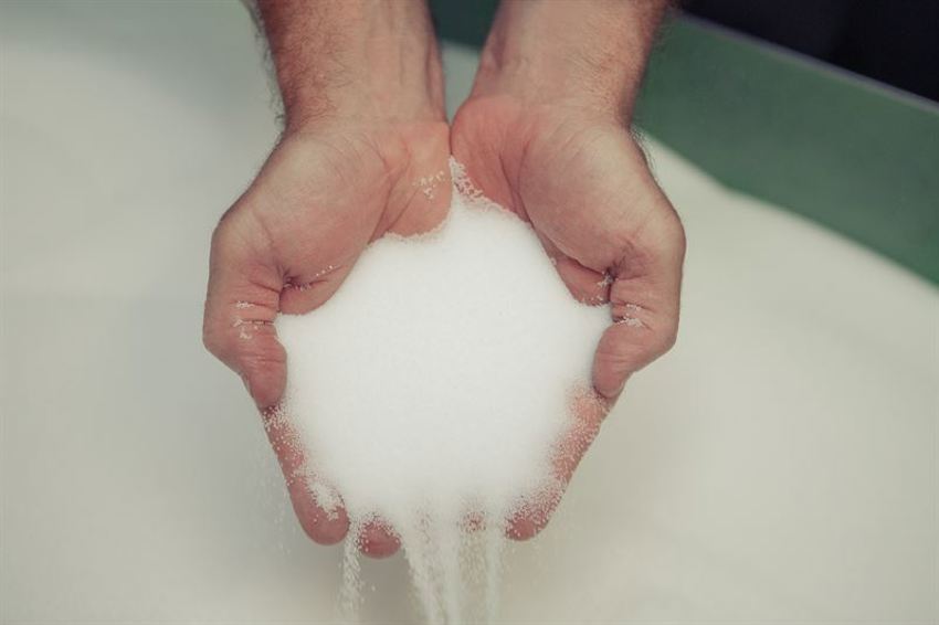 Foto van 2 handen die witte EPS grondstof vasthouden boven een bak met grondstof. 