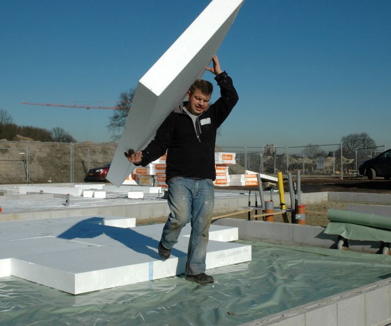 Projectfoto van een verwerker die een vloerplaat draagt op de bouwplaats waar al vloerplaten liggen.