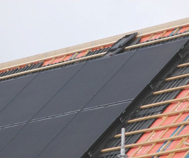 Close-up van de nok met oranje dakelementen en daarop een aantal solar modules en zonnepanelen.