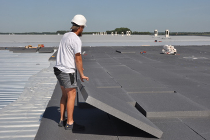 Een verwerker legt EPS-HR isolatieplaten in een dubbele laag op het dak van het distributiecentrum.