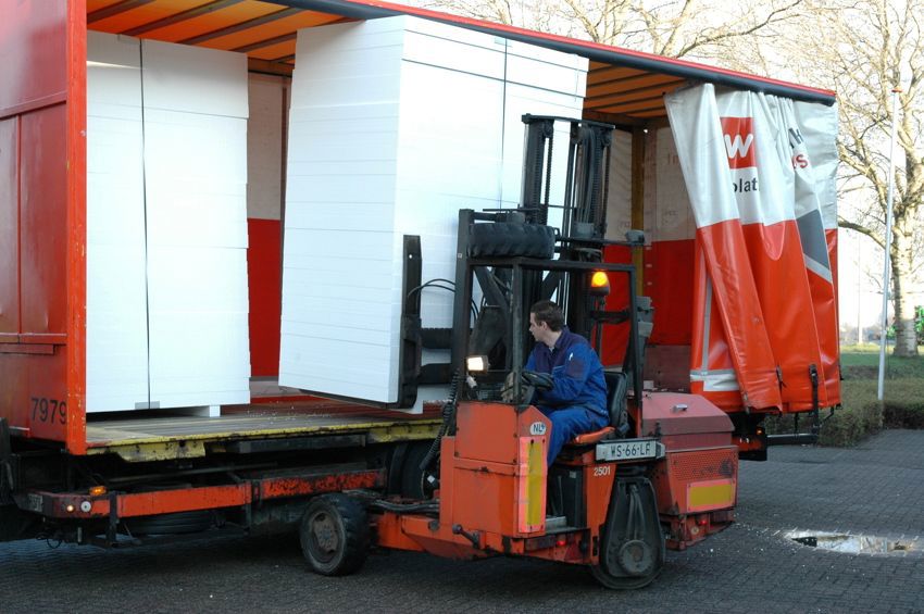 Foto van een chauffeur die een stapel witte EPS isolatieplaten uit de vrachtwagen lost of laadt. 
