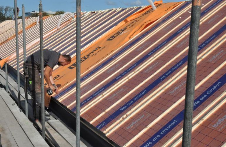 Projectfoto van een dakdekker die SlimFix Reno+ isolatieplaten bevestigd op een dragend dakbeschot. 