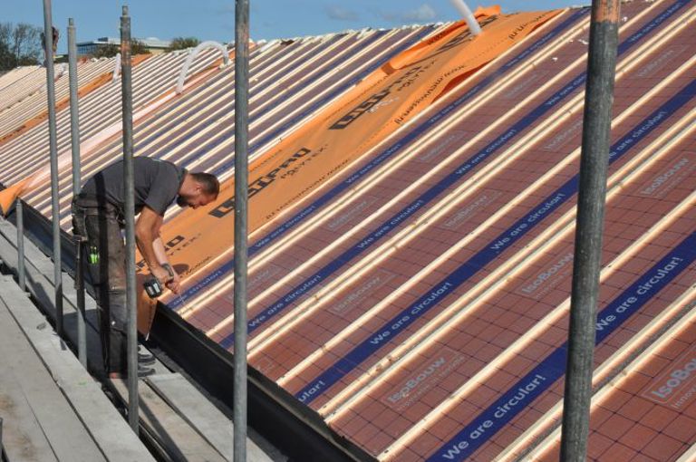 Projectfoto van een dakdekker die SlimFix Reno+ isolatieplaten bevestigd op een dragend dakbeschot. 