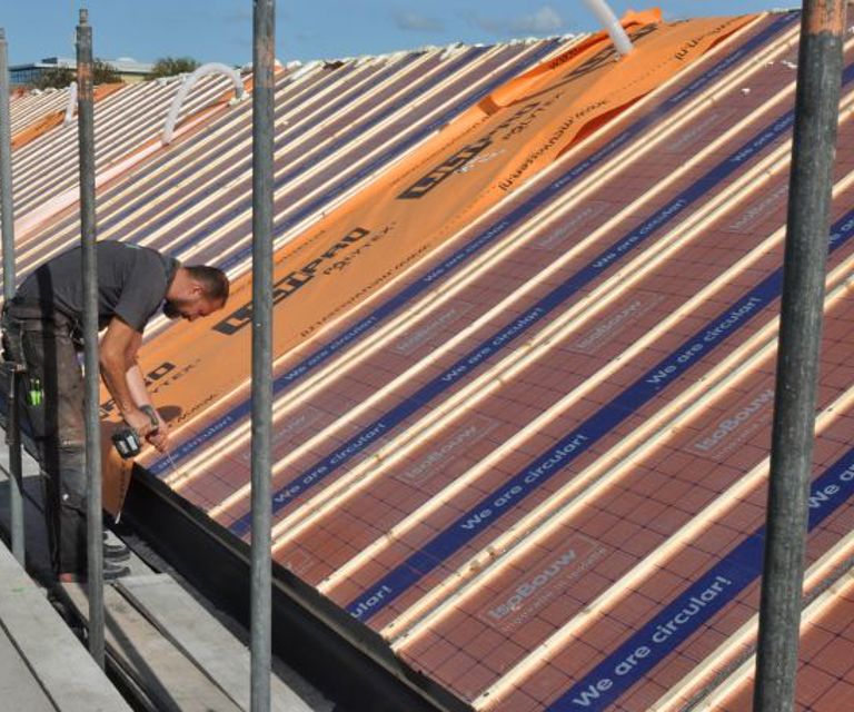 Projectfoto van een dakdekker die SlimFix Reno+ isolatieplaten bevestigd op een dragend dakbeschot. 