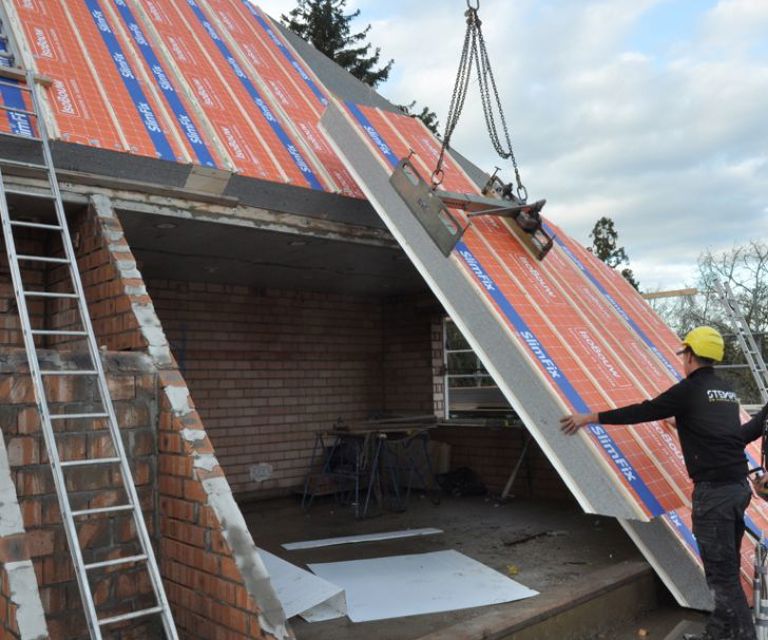 Projectfoto van een dakdekker die een SlimFix XT Passief dakpaneel plaatst m.b.v. een hijsklem.