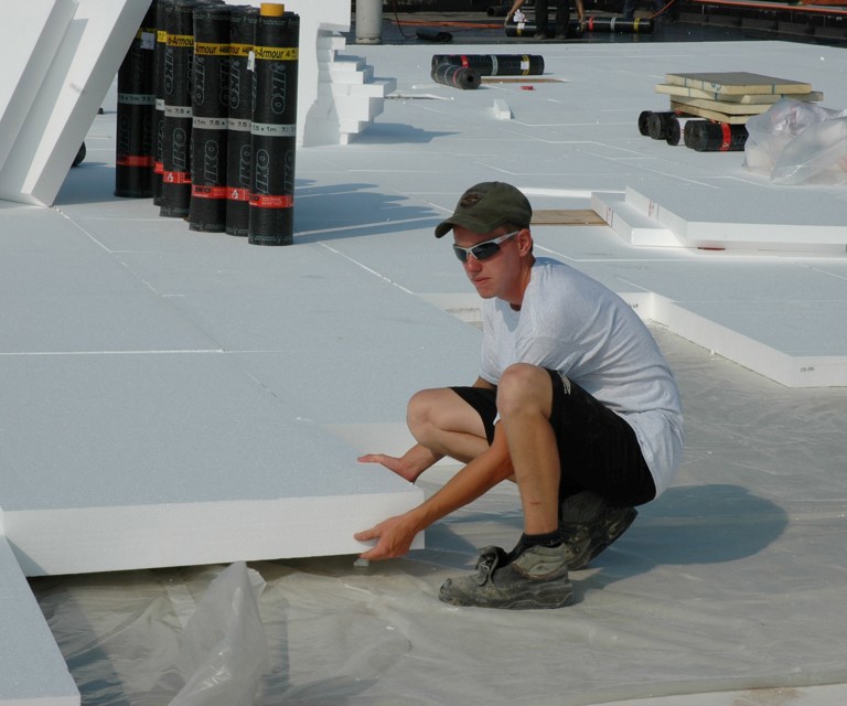 Projectfoto van een verwerker die een witte EPS isolatieplaat plaatst op een plat dak van een gebouw