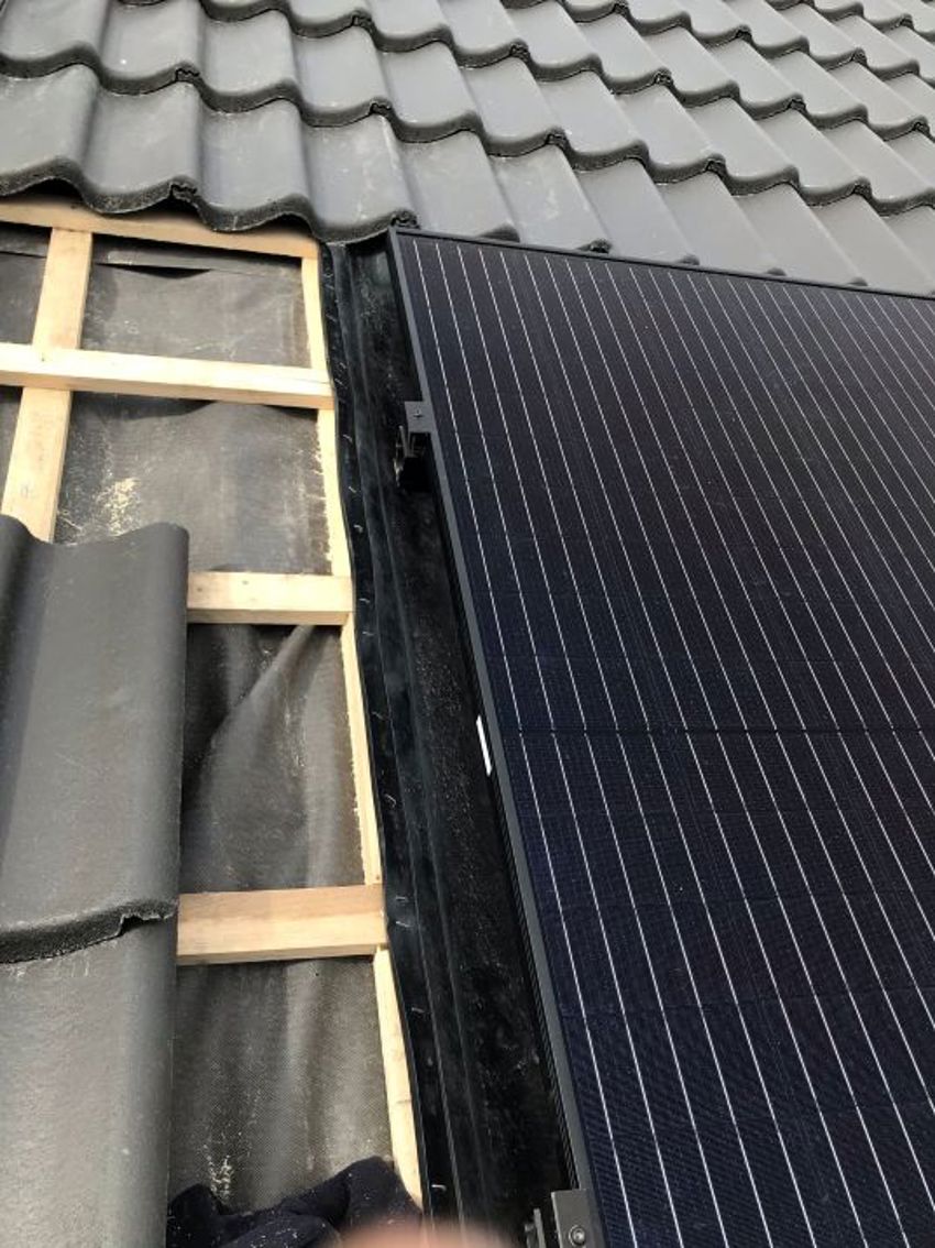 Close-up van een hellend dak waar zonnepanelen en dakpannen liggen, een gedeelte ligt nog open. 