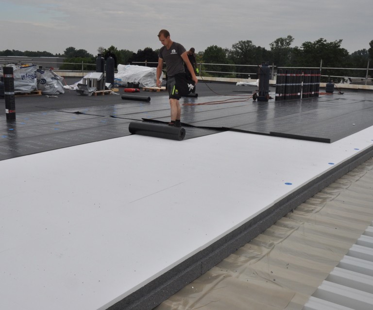 Projectfoto van een platdak waar een folie wordt uitgerold op de PowerTop Protect isolatieplaten. 