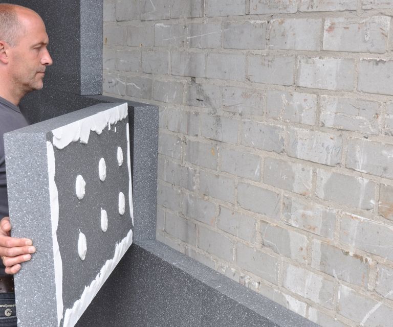 Projectfoto van een verwerker die de PolyStuc buitengevelisolatieplaat plaatst tegen de buitenmuur. 
