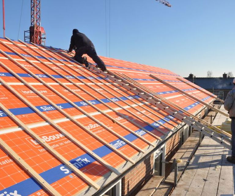 Projectfoto van een dakdekker die op een dak met SlimFix Spoor isolatieplaten staat met panlatten.