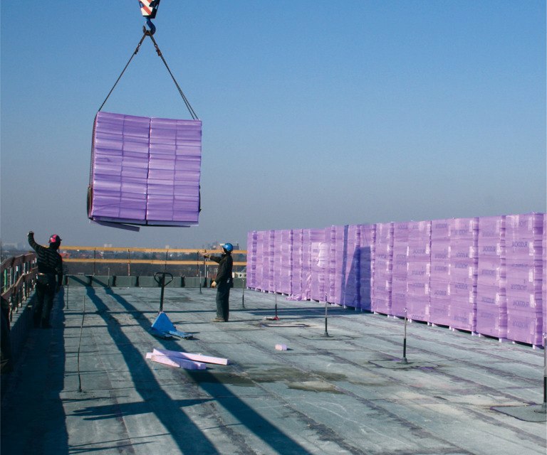 Projectfoto van een hijskraan die een stapel XPS isolatieplaten lost op het platte dak. 