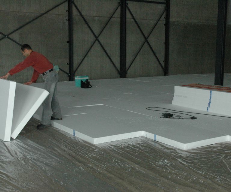 Projectfoto van een verwerker die een vloerplaat legt in een hal waar al vloerplaten liggen.