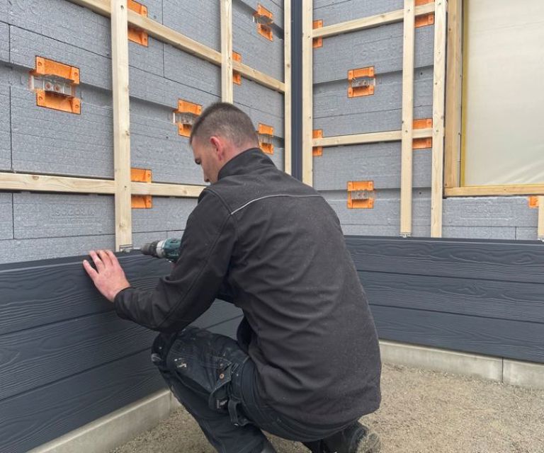 Projectfoto van een man die gevelbekleding monteert op hout van het SlimFort gevelisolatiesysteem.